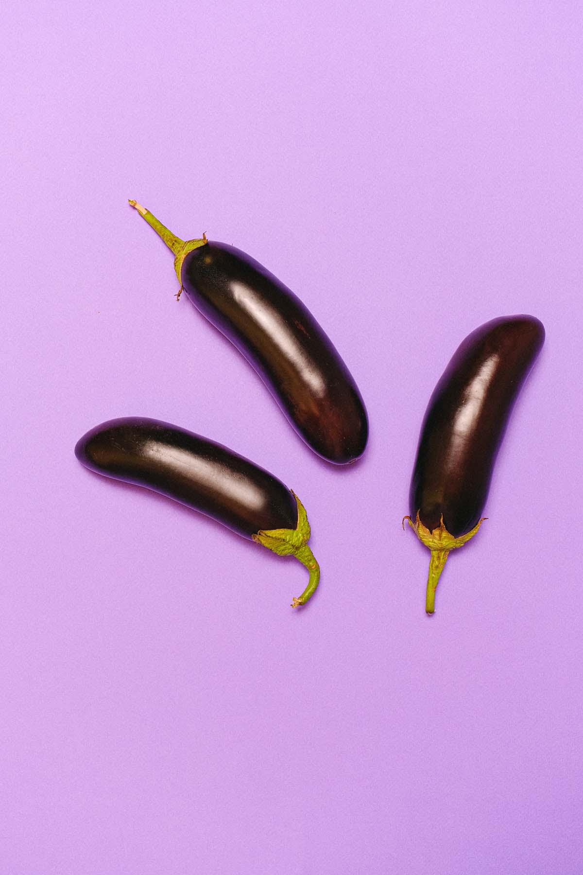 Three large eggplants on a lilac background.